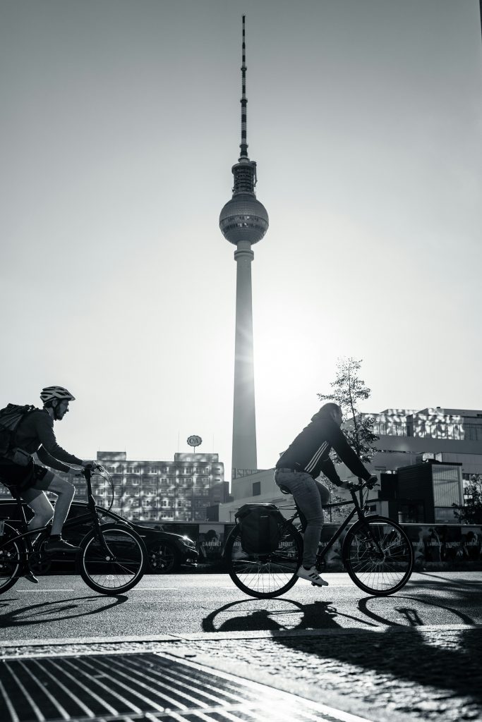 Zwei Fahrradfahrer fahren durch Berlin mit dem Fernsehturm-Panaroma im Hintergrund.