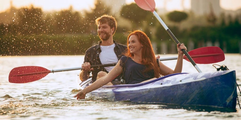 Confident young caucasian couple kayaking on river together with sunset in the backgrounds. Having fun in leisure activity. Romantic and happy woman and man on the kayak. Sport, relations concept.