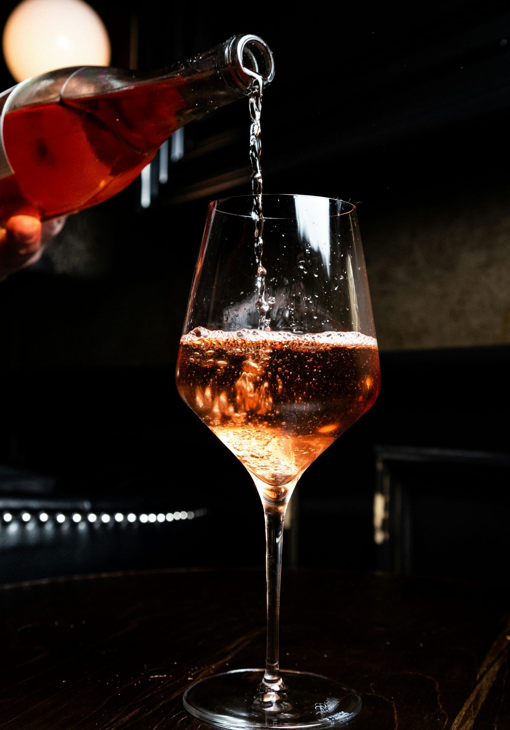 Roséwein wird in ein Weinglas eingegossen, das auf einer schwarzen Theke in einem Restaurant steht.
