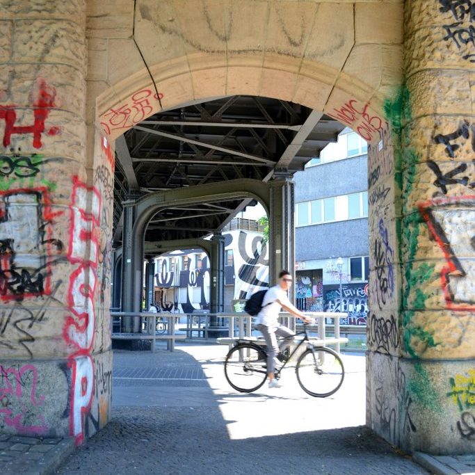 Radfahrer, der unter S-Bahn-Brücke in Berlin entspannt im Sommer entlangfährt, um Berlin zu erkunden.